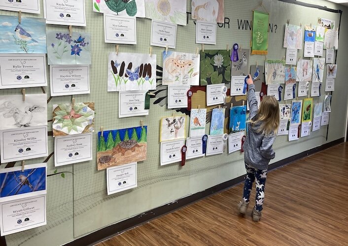 A young artist points to her entry in the 2023 Ohio Wildlife Youth Art Show.