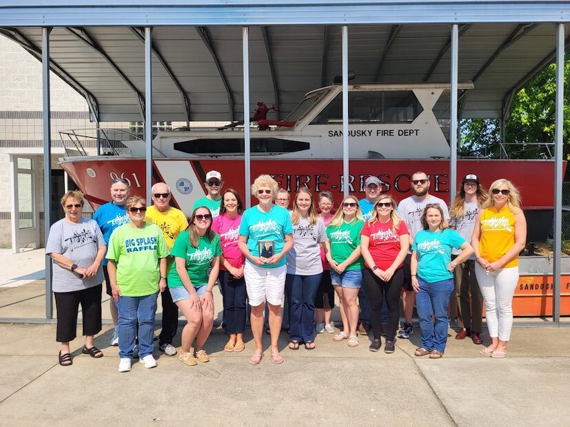 Members of Dean Howman's family, including Dean's widow, Candy (holding a photo of Dean), pose for a photo in front of the Maritime Museum's Howman Boat House. 